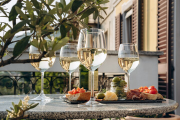 Outdoor dining or aperitif white wine glasses on a stone table with gourmet charcuterie board assorted meats, olives, and cheese