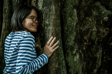 Woman practicing forest therapy mindfulness meditation leaning face against tree trunk. Digital...