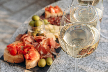 Outdoor dining or aperitif white wine glasses on a stone table with gourmet charcuterie board assorted meats, olives, and cheese