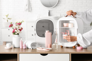 Female hands taking cream from small refrigerator for cosmetic products. Closeup