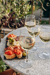 Outdoor dining or aperitif white wine glasses on a stone table with gourmet charcuterie board assorted meats, olives, and cheese