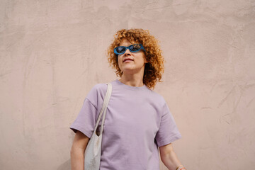 Stylish woman with sunglasses and tote bag near pink wall