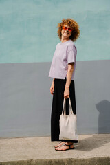 Mature woman with curly hair and eco bag near colorful wall
