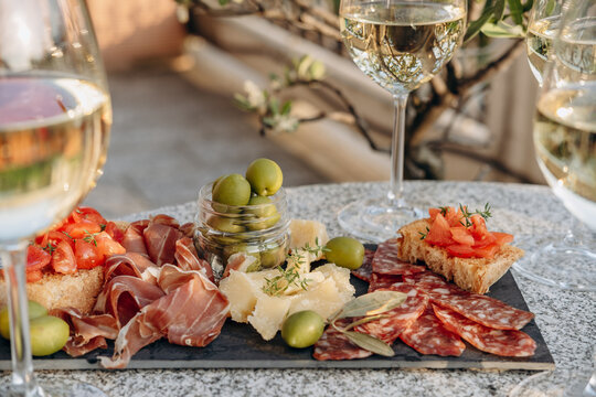 Gourmet charcuterie board with meats prosciutto ham, salami, green olives and cheese with white wine or prosecco aperitif or dinning outdoor Italian style
