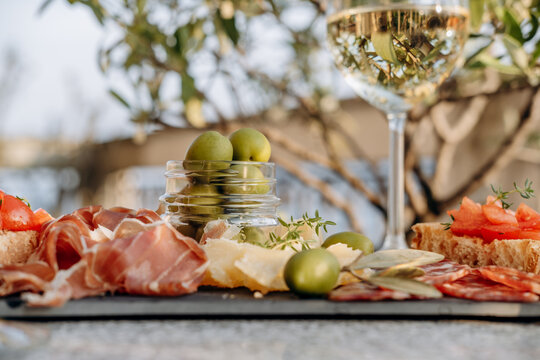 Gourmet charcuterie board with meats prosciutto ham, salami, green olives and cheese with white wine or prosecco aperitif or dinning outdoor Italian style