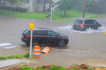 Vehicles struggle to navigate flooded streets during heavy rainstorm in residential neighborhood.