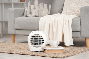 Electric fan heater with cup of tea and books on rug in living room