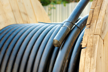 Large black utility cable coiled tightly on wooden spool for electrical or fiber optic...