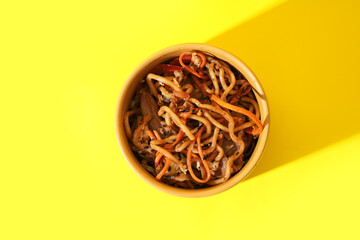 Bowl of tasty Chinese noodles with vegetables and meat on yellow background