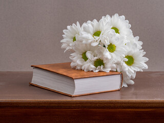 a bouquet of chamomile flowers and old books on a table on a natural background. a composition with books in a rustic style. the concept of reading and relaxing. the summer season. template for regist