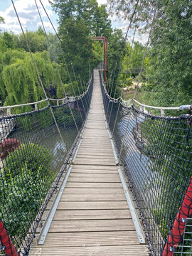 Fototapeta Perspective view of a suspension rope bridge (monkey bridge) entrance crossing over a river, highlighting the structure’s length and natural surroundings