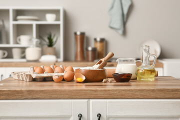 Bowl of flour with eggs, scoop, jug of milk and oil for preparing dough on kitchen counter