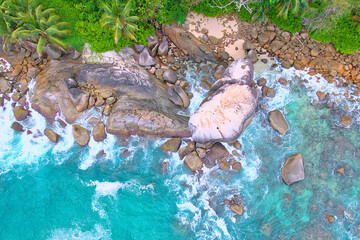 Drone shot of granite stones, wavy ocean, with pink sand, lush vegetation, Mahe Seychelles 1