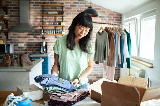 Asian woman unpacking clothes from a delivery box at home boutique