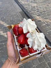 Close-up of a person holding a tray with a Belgian waffle topped with whipped cream, strawberries,...