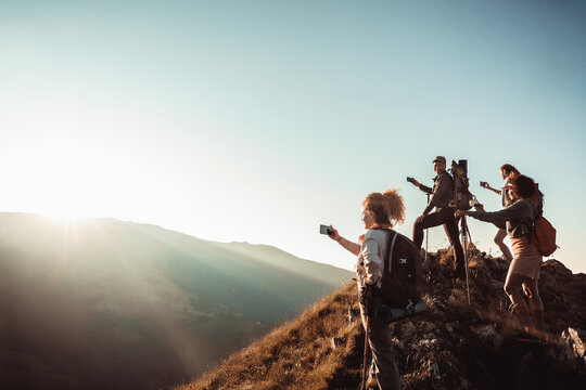 Young and diverse group of female friends taking a picture of a view with their smart phones while hiking in the mountains and hills