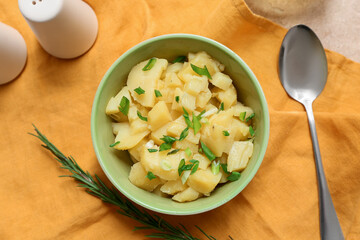 Bowl of tasty potato salad with green onion, rosemary and spoon on napkin
