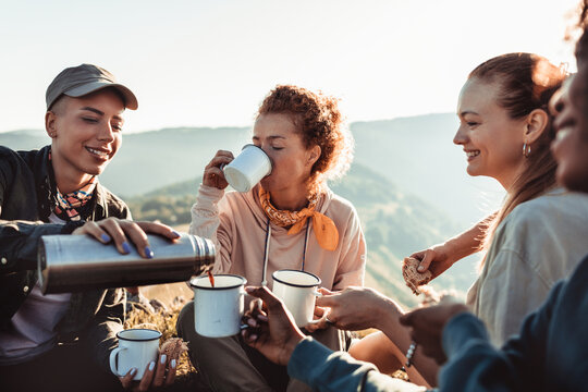 Young diverse group of female friends having a coffee break after hiking in the hills and mountains