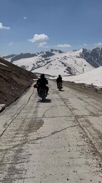 Vertical video showing close-up of touring bikers on powerful Dominar bikes heading towards Burzil Top. Mountain road, high-altitude scenery, and dramatic peaks create stunning adventure visuals.

