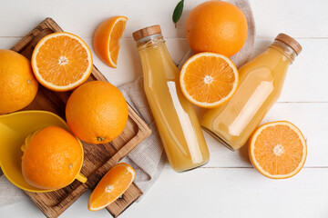 Oranges with juicer and glass bottles of tasty juice on white wooden background