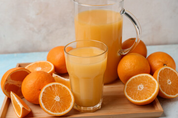 Oranges with glass and jug of tasty juice on light background