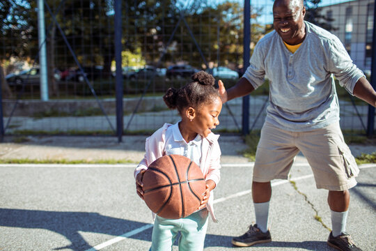 Father teaching daughter how to play basketball outdoors