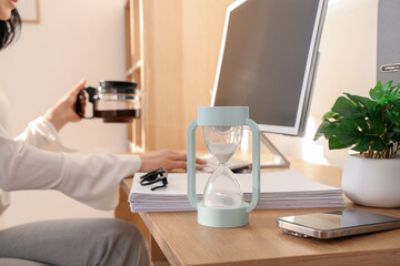 Hourglass on desk against businesswoman with coffee pot in office, closeup