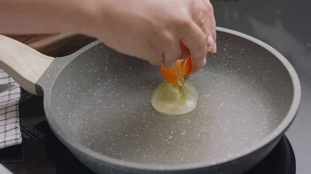 Process of breaking an egg on a frying pan for cooking sunny side up fried egg.