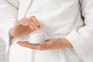 Young woman with jar of cosmetic cream on light background, closeup