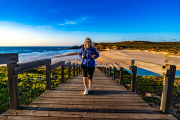 Beautiful middle aged woman hiking on tourist trail along atlantic ocean in nature park Vicentine Coast in Portugal on spring day. Amoreira beach. Front view