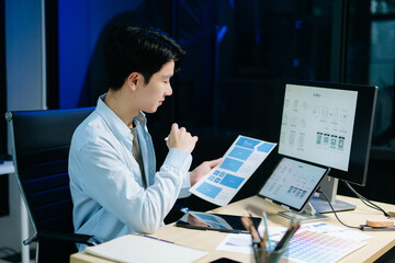 Asian male designer pointing at UX wireframes on screen and tablet in modern office. Ideal for...