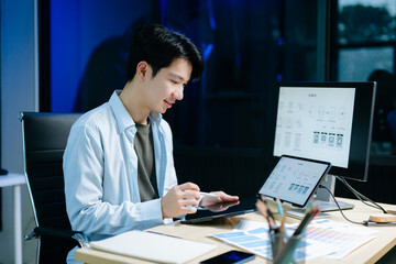 Asian male designer pointing at UX wireframes on screen and tablet in modern office. Ideal for...