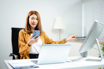 Confident Asian business people using laptops, tablets, and phones in modern office workspace,...