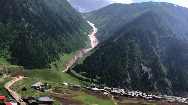 A stunning mountain valley in Minimarg, skardu, featuring a blue river, traditional village houses, snow-covered peaks, lush green hills &mdash; captured in motion during a peaceful travel journey.
