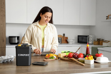 Young woman cutting food with container for compost in kitchen