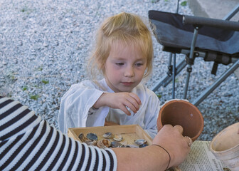 A young girl concentrates on gluing sea shells to a clay pot during a hands-on outdoor craft...