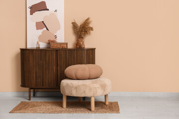 Interior of living room with pouf and home decor on commode near brown wall