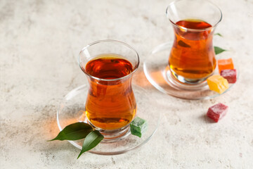 Glasses of Turkish tea with delights and leaves on light grunge background