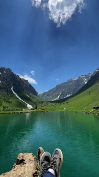 POV shot of a hiker relaxing at Rainbow Lake, Domail Baltistan, Pakistan. Alpine turquoise water, snow-capped peaks, green valleys. Perfect for travel concepts, adventure, and outdoor relaxation. 