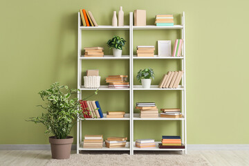 Shelving unit with books, decor and houseplants near green wall in room © Pixel-Shot