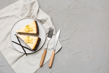 Plate with pieces of sweet vanilla cheesecake on grey background