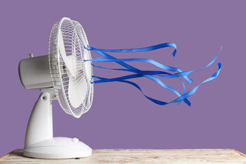 Electric fan with fluttering ribbons on table against violet background