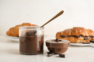 Jar with melted chocolate and sweet croissants on white background