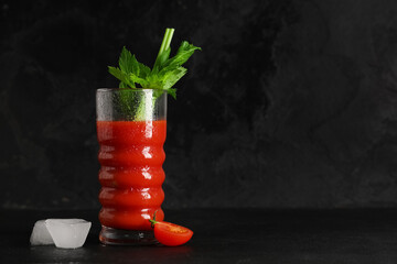 Glass of bloody mary with celery, cut tomato and ice cubes on black grunge background