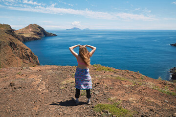 Woman standing on a cliff overlooking the vast ocean and coastal landscape with islands in the distance under a blue sky