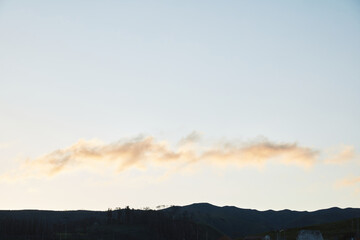 Soft cloud formation over dark hills at dawn or dusk, capturing the serene landscape with subtle light