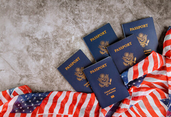 Five United States passports lie on gray surface beside American flag, symbolizing national...