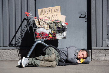 Homeless man with his things in shopping cart sleeping on street