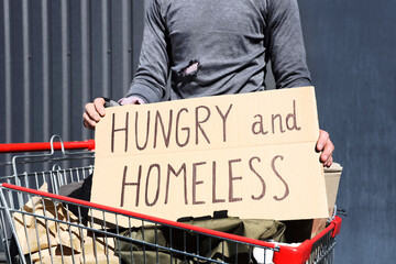 Homeless man with cardboard and shopping cart on street
