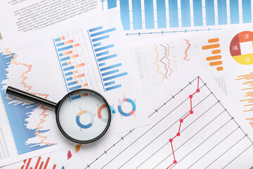Magnifier with many business graphics and diagrams as background, closeup